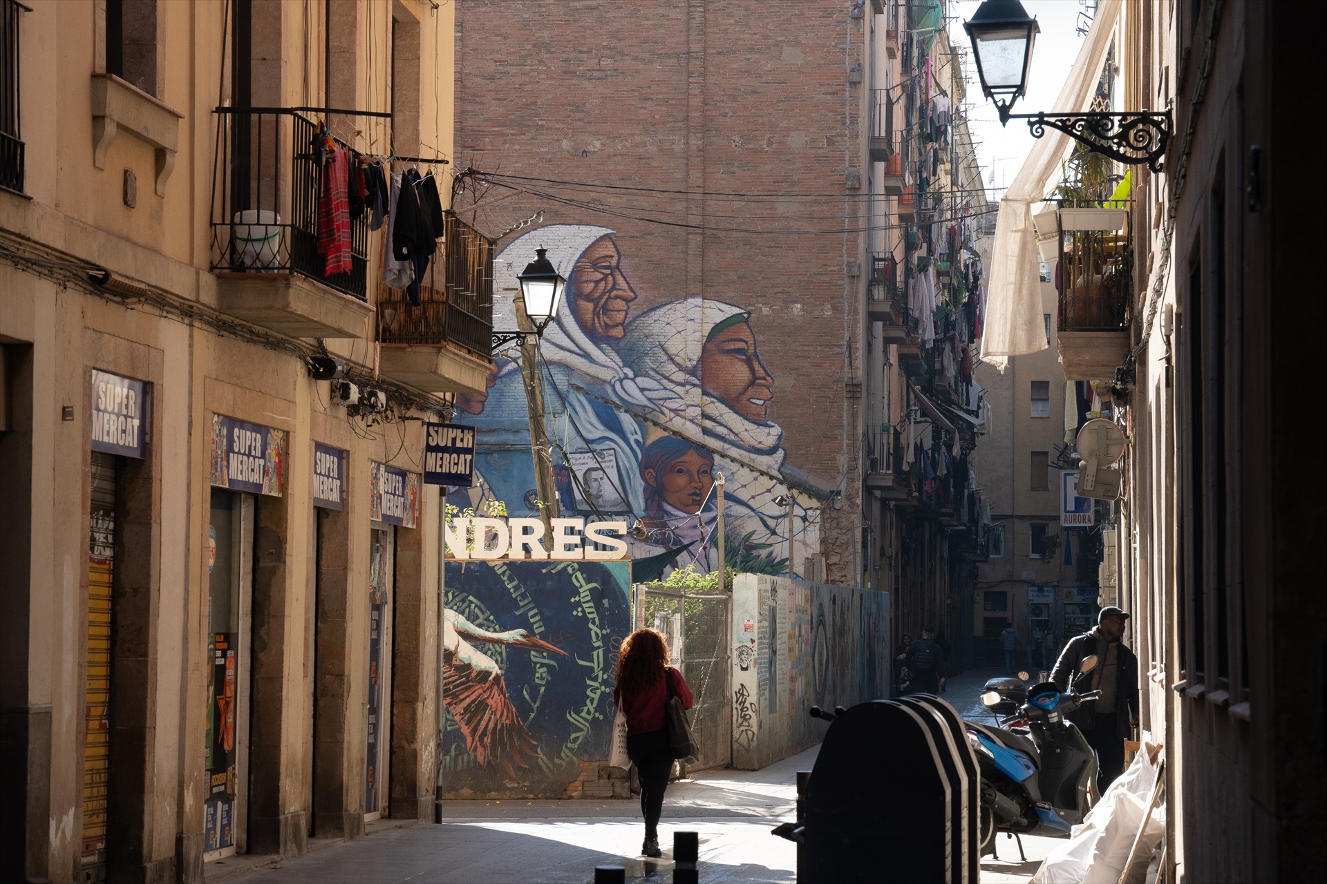 Dos personas caminan por una calle céntrica, a 24 de enero de 2024, en Barcelona, Catalunya (España), frente a un mural que presenta a personas migrantes.- David Zorrakino / Europa Press