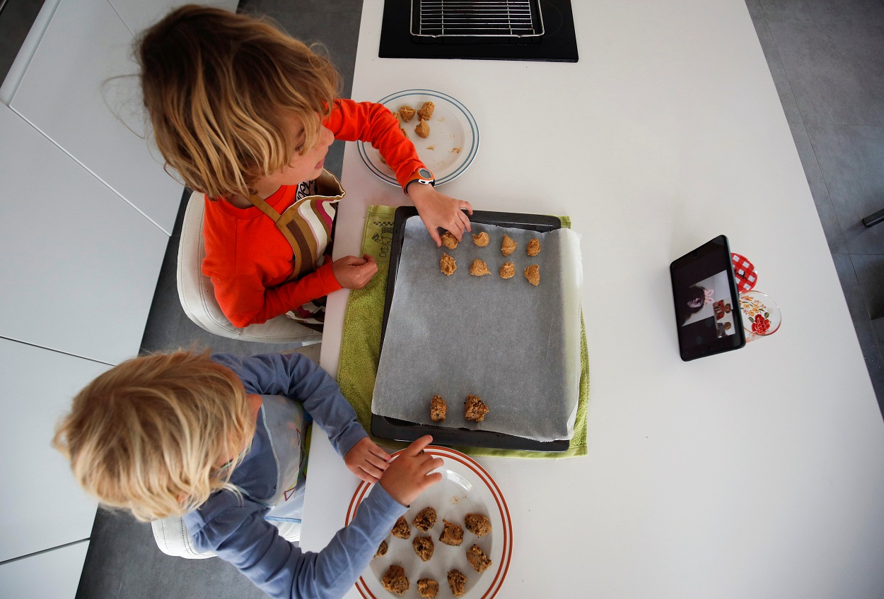 Unos niños preparan unas galletas siguiendo la receta que les dan sus abuelos a través de una 'tablet'. REUTERS/Albert Gea