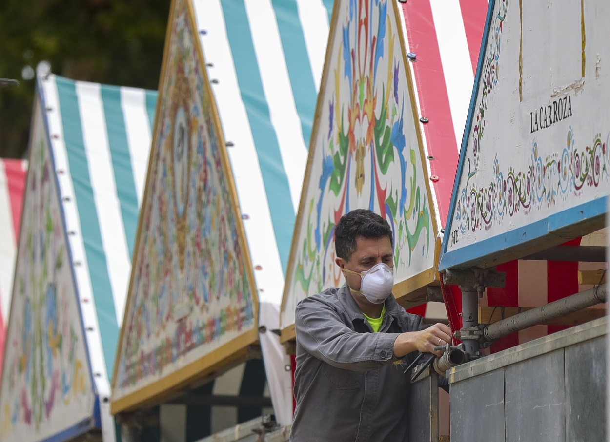 Un operario con mascarilla desmonta una caseta en las instalaciones de la Feria de Abril de Sevilla. EUROPA PRESS/María José López