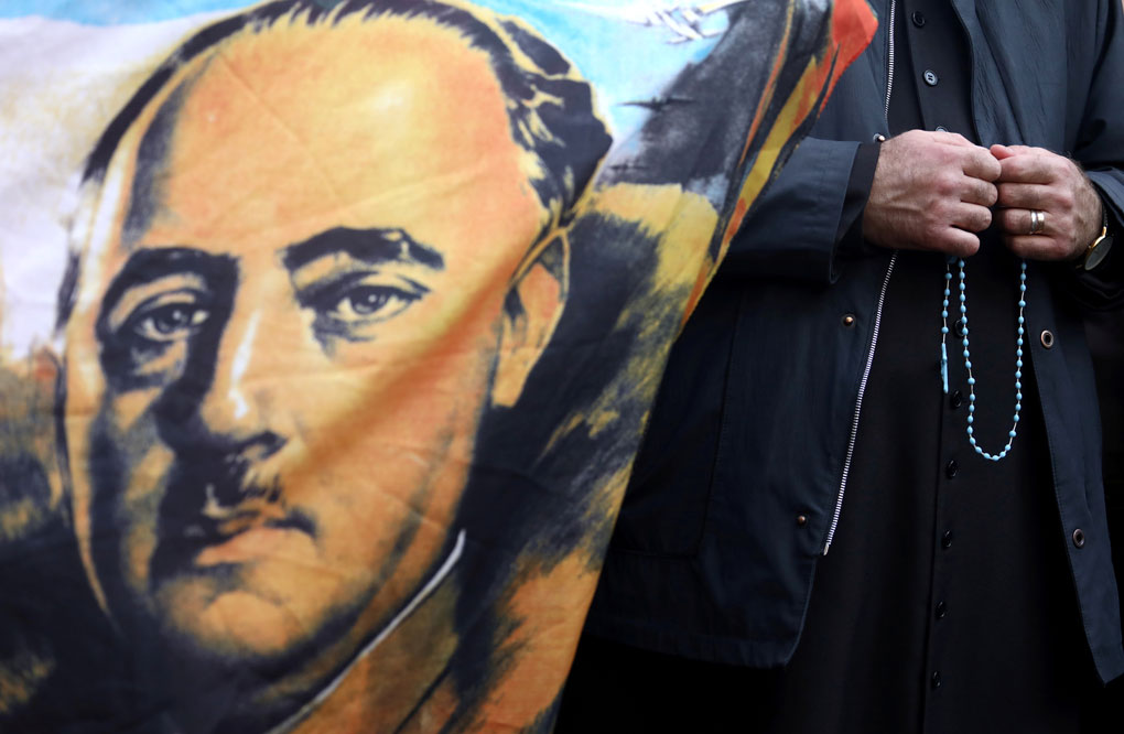 Un sacerdote sostiene un rosario junto a una bandera con el retrato del dictador Francisco Franco, en las afueras del cementerio Mingorrubio-El Pardo, el 24 de octubre. REUTERS / Sergio Perez