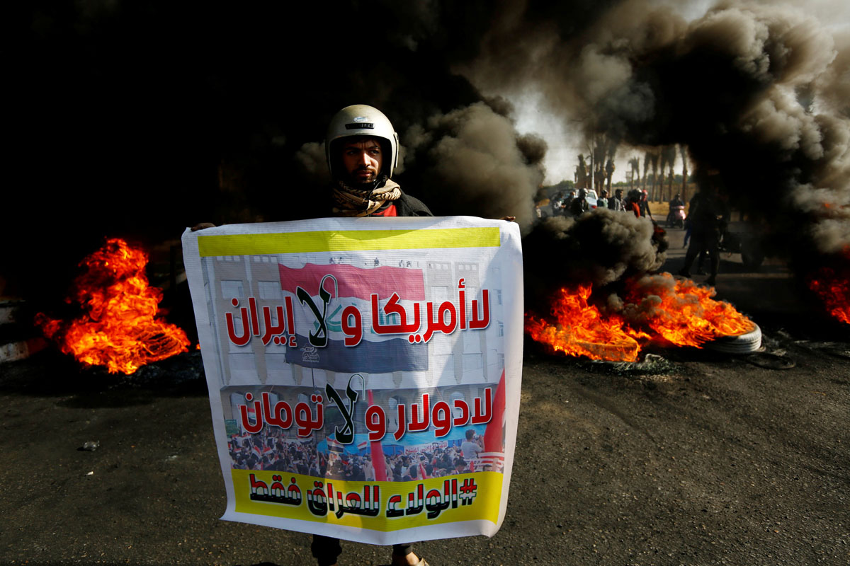 Un manifestante iraquí lleva un cartel que dice: "No Estados Unidos ni Irán, No dólar y No Toman, lealtad solo a Irak" junto a la quema de neumáticos para bloquear una carretera durante las protestas contra el gobierno en Najaf. REUTERS / Alaa al-Marjani
