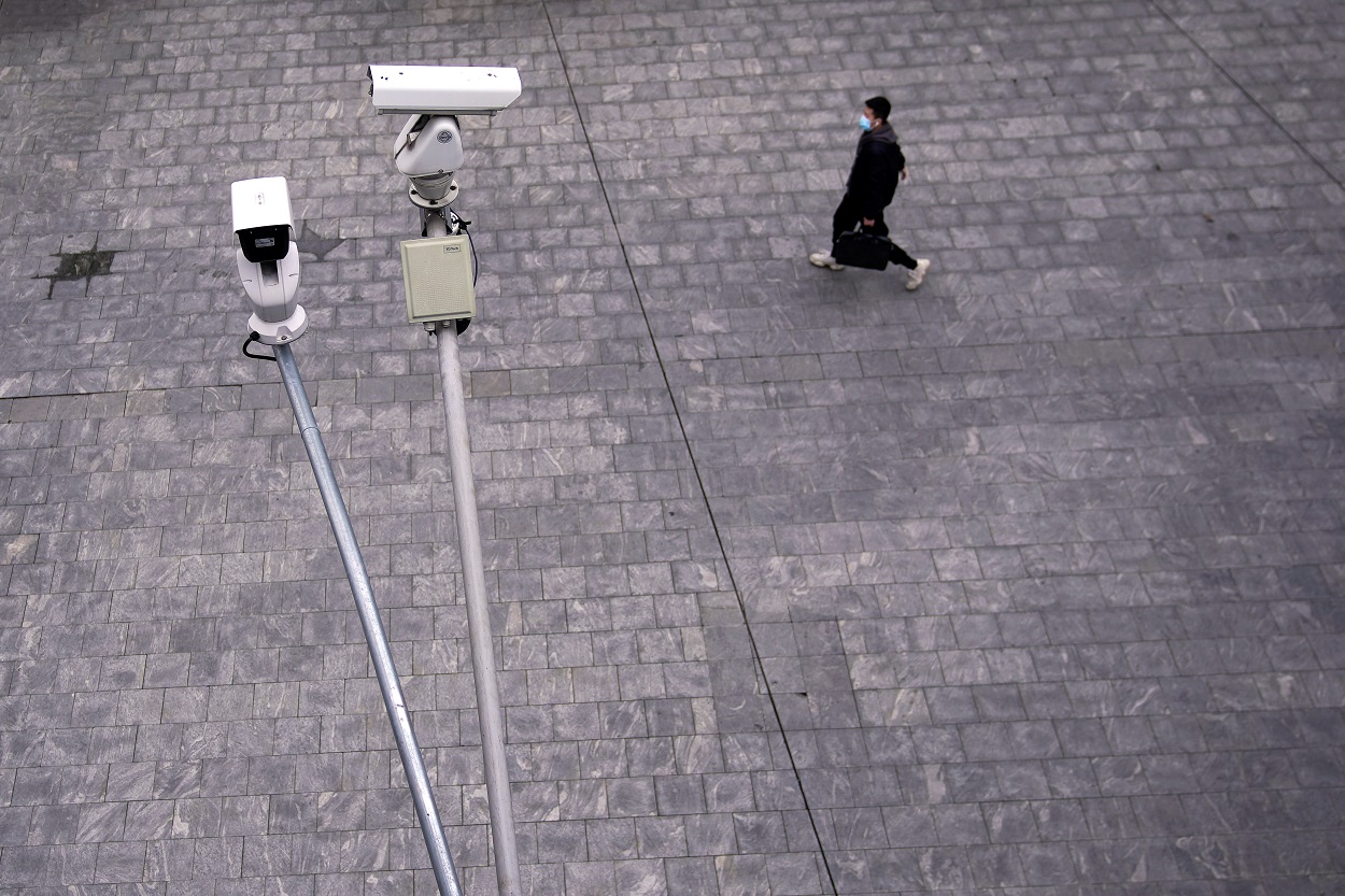 Un hombre con mascarilla camina por Shanghai, bajo unas cámaras de vigilancia en la calle. REUTERS/Aly Song
