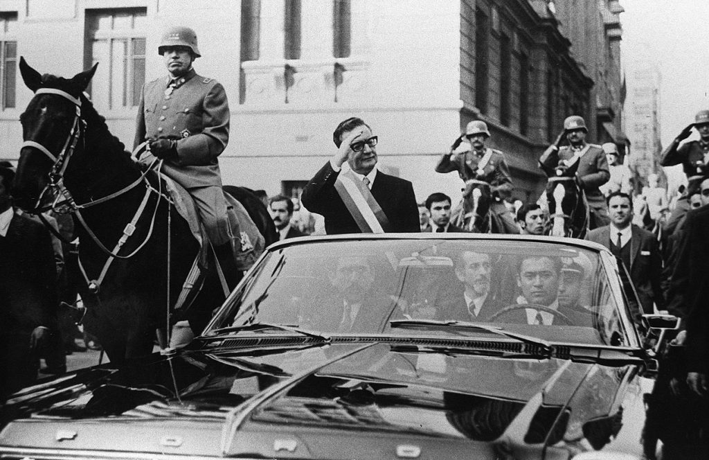 El presidente de Chile, Salvador Allende, saluda a sus seguidores desde su coche descubierto, en Santiago, pocas semanas después de su elección. A su lado, a caballo, es escoltado por el general Augusto Pinochet. | AFP