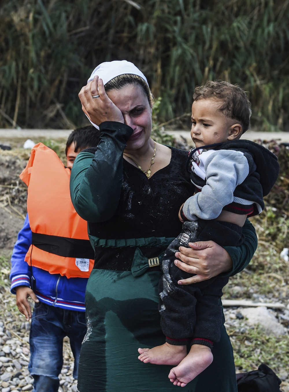 Una mujer afgana con un niño en brazos se emociona tras lograr alcanzar la costa a bordo de una lancha neumática en la isla de Lesbos (Grecia). EFE/Filip Singer