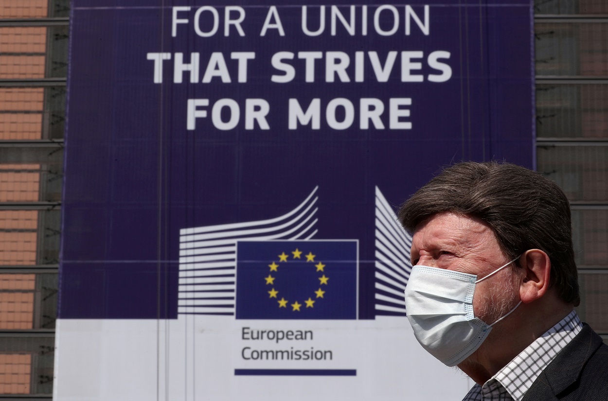 Un hombre con mascarilla para por delante de la sede de la Comisión Europea en Bruselas, donde cuelga un cartel con el lema "Por una Unión que se esfuerza por lograr más". REUTERS/Yves Herman