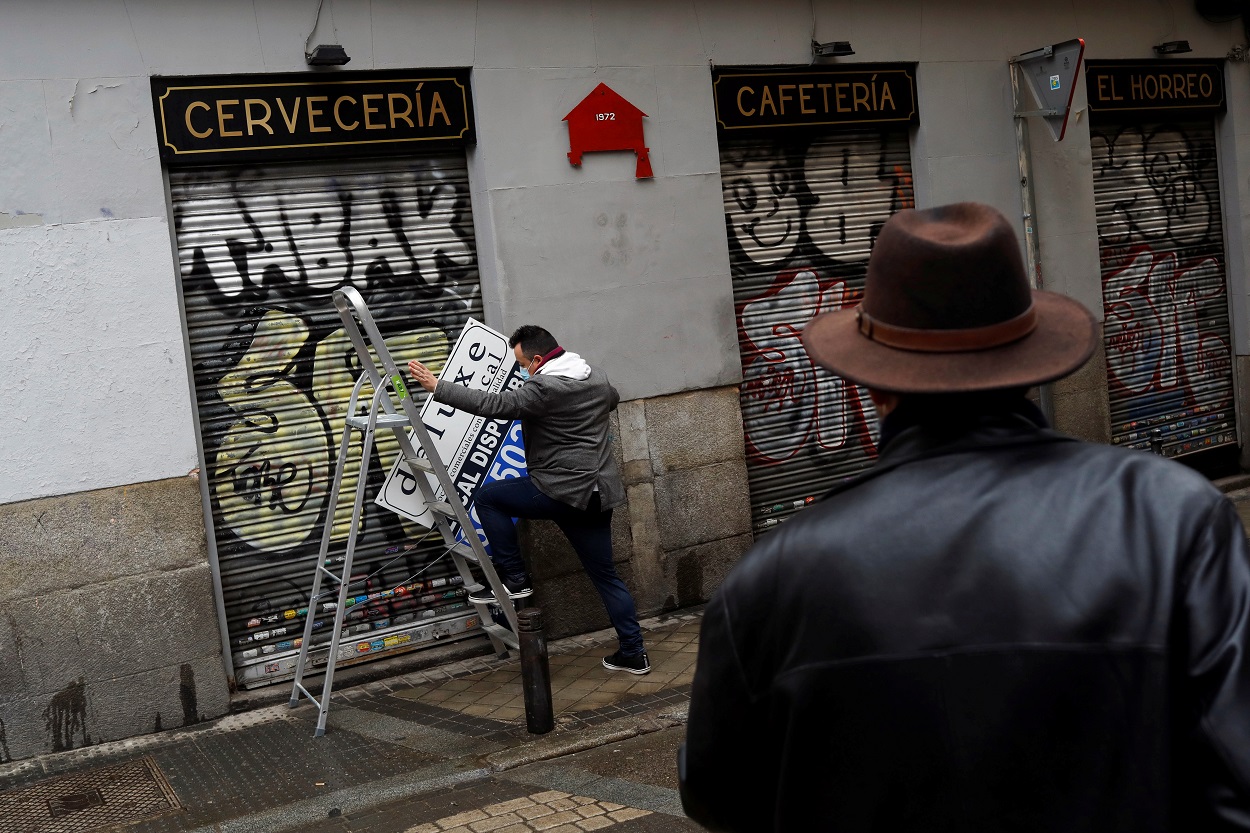 Un hombre se prepara para colgar el cartel de 'Disponible' en el local de una cafetería cerrada durante la pandemia del coronavirus, en el centro de Madrid. REUTERS/Susana Vera