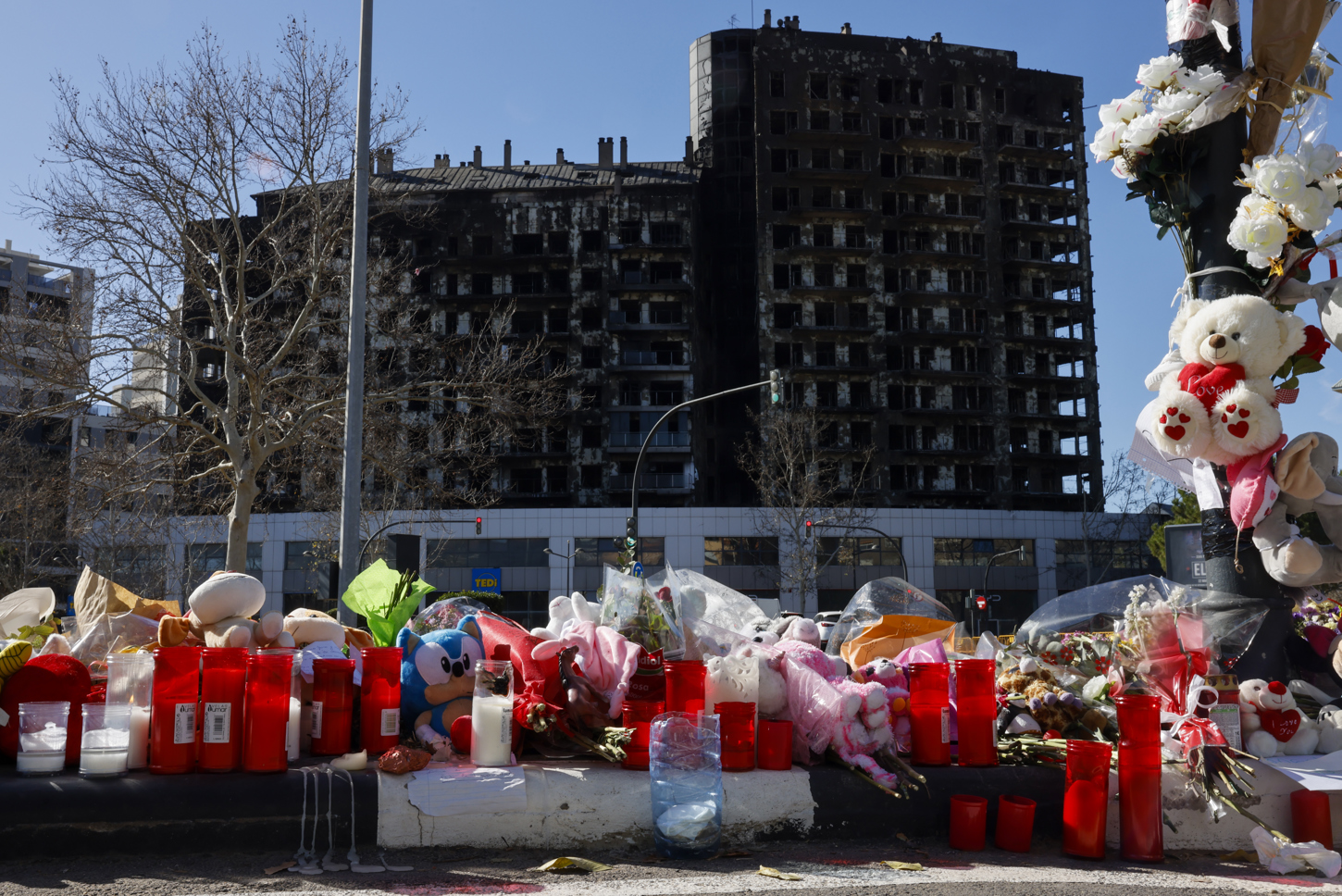 Detalle de flores, velas y peluches colocados a modo de homenaje ante el edificio incendiado en el barrio de Campanar de València en el que murieron diez personas y deja más de 400 damnificados. EFE/Ana Escobar