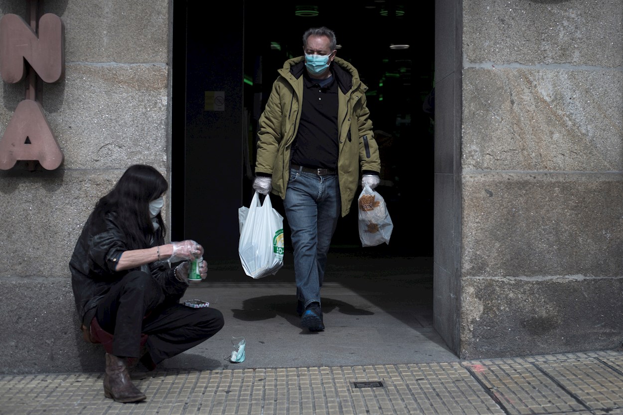 Un hombre pasa ante una mujer sin recursos a la salida de un supermercado en Ourense. EFE/Brais Lorenzo