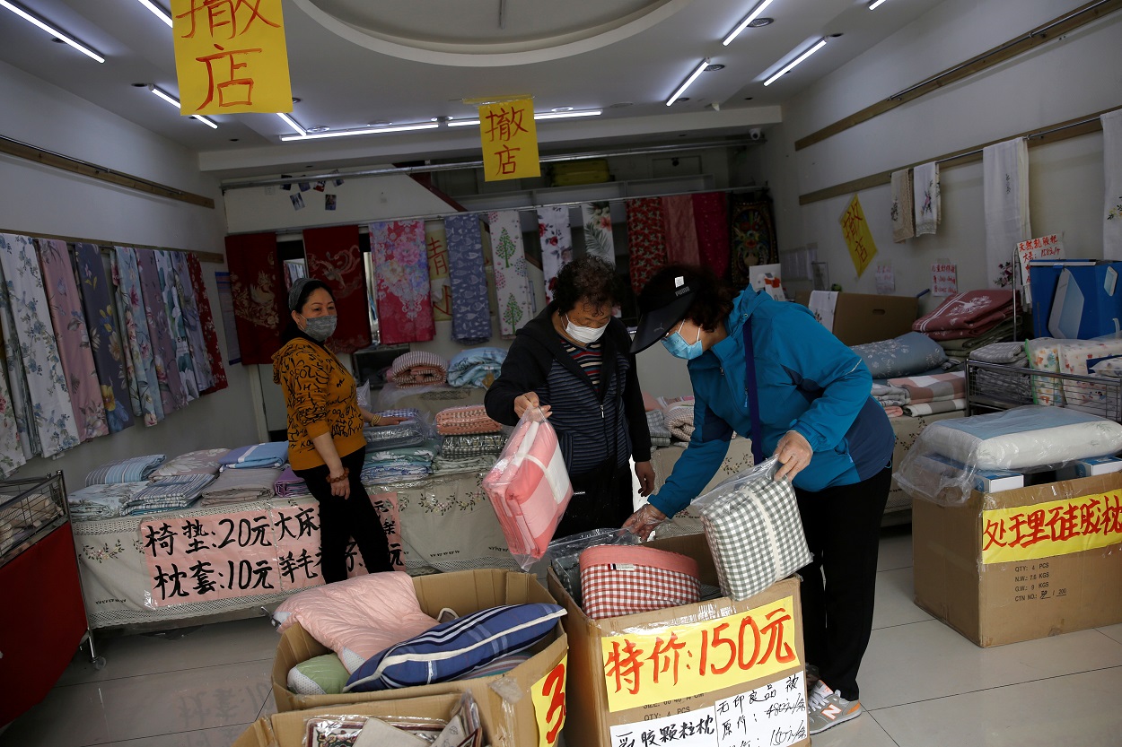 Unos clientes con mascarillas compran ropa de cama en una tienda de ropa para el hogar con avisos de liquidación, en Pekín.. REUTERS / Tingshu Wang