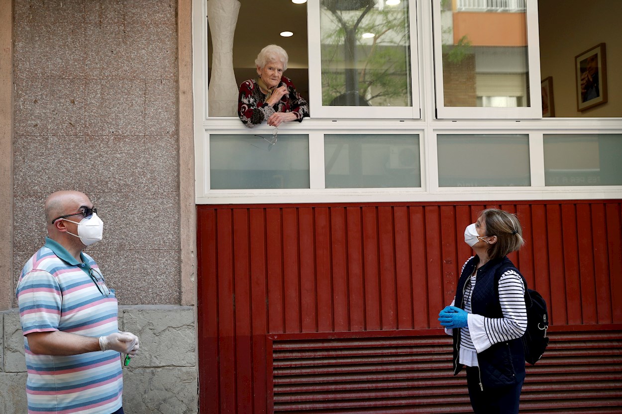 Una anciana, usuaria de una residencia geriática de L'Hospitalet de Llobregat (Barcelona), habla desde una ventana con una hija y un amigo de la familia. EFE/Toni Albir