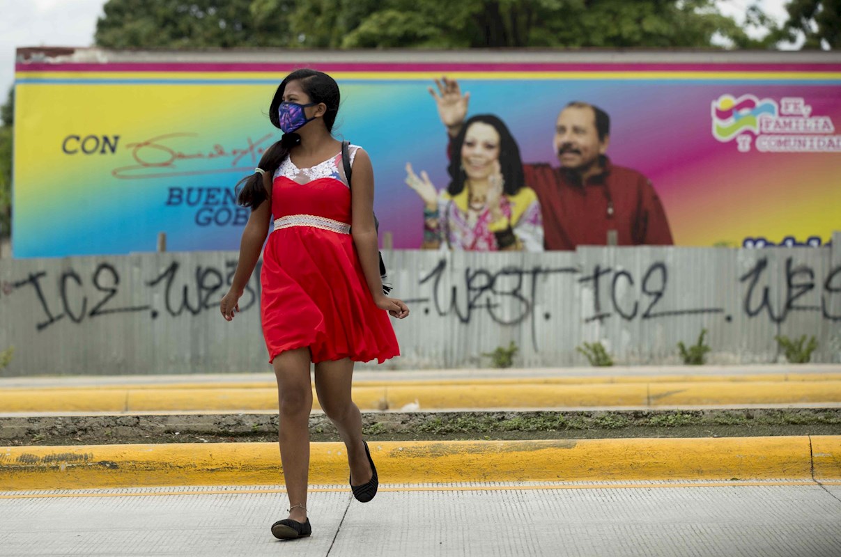 Una joven con mascarilla pasa frente a un cartel del presidente de Nicaragua Daniel Ortega y su esposa Rosario Murill, en Managua. EFE/Jorge Torres