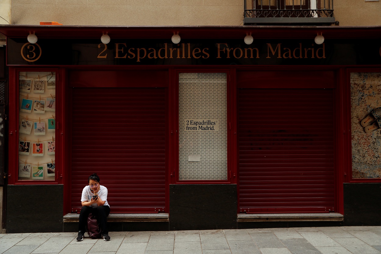 Una joven mira su móvil, sentada en la puerta de una tienda cerrada en el centro de Madrid. REUTERS/Susana Vera