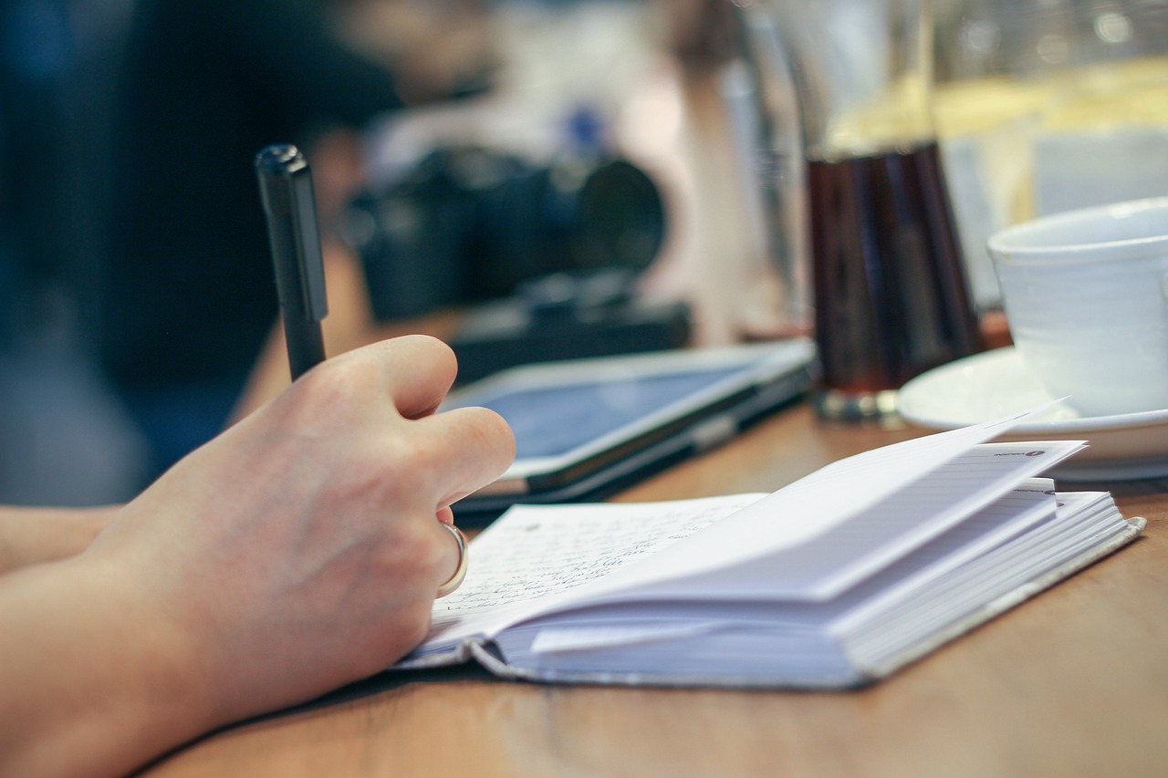 Una persona escribiendo en su libreta en un bar. / Pixabay
