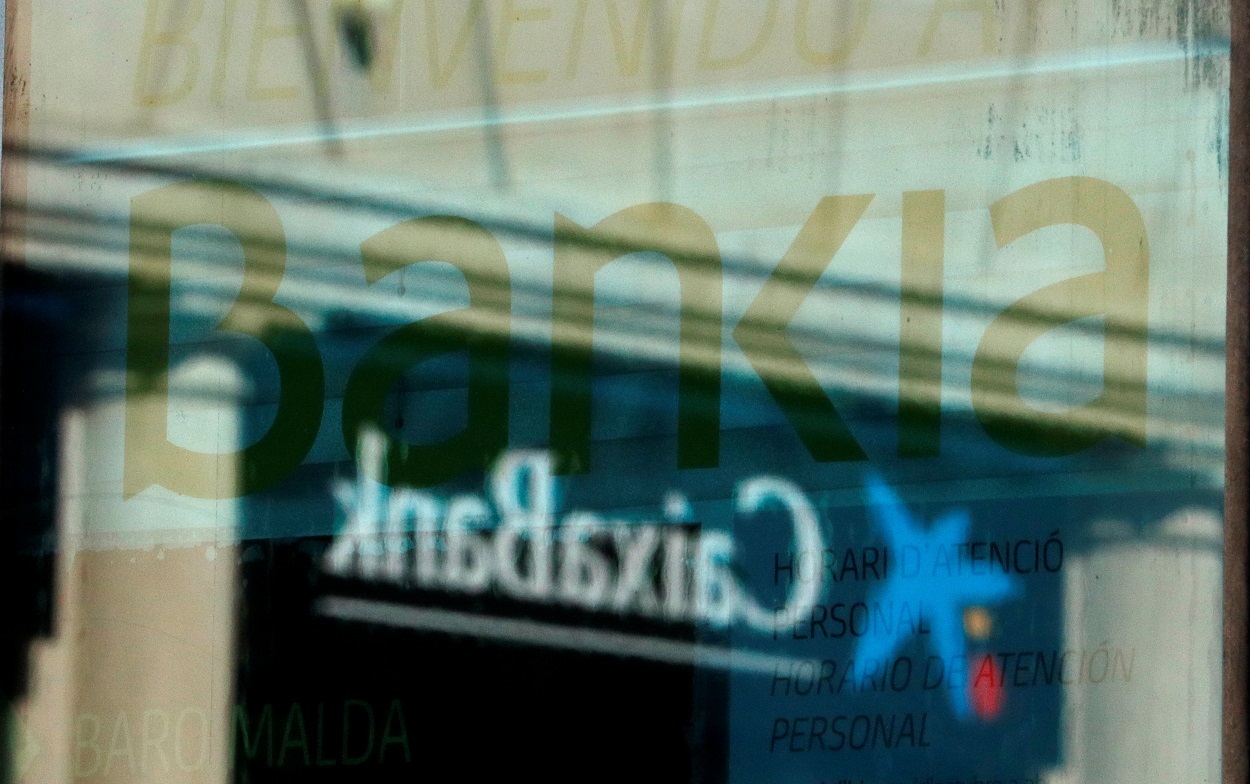 El logo de una oficina de Caixabank se refleja en la ventana de una sucursal de Bankia, en Barcelona. REUTERS/Albert Gea